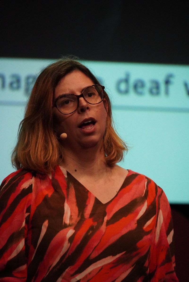 Je suis en train de donner une conférence au DevFest Nantes. Je porte un haut coloré de plusieurs variantes de rouge et j'ai un serre-tête en guise de micro. Derrière moi, on voit le mot deaf d'un de mes slides.