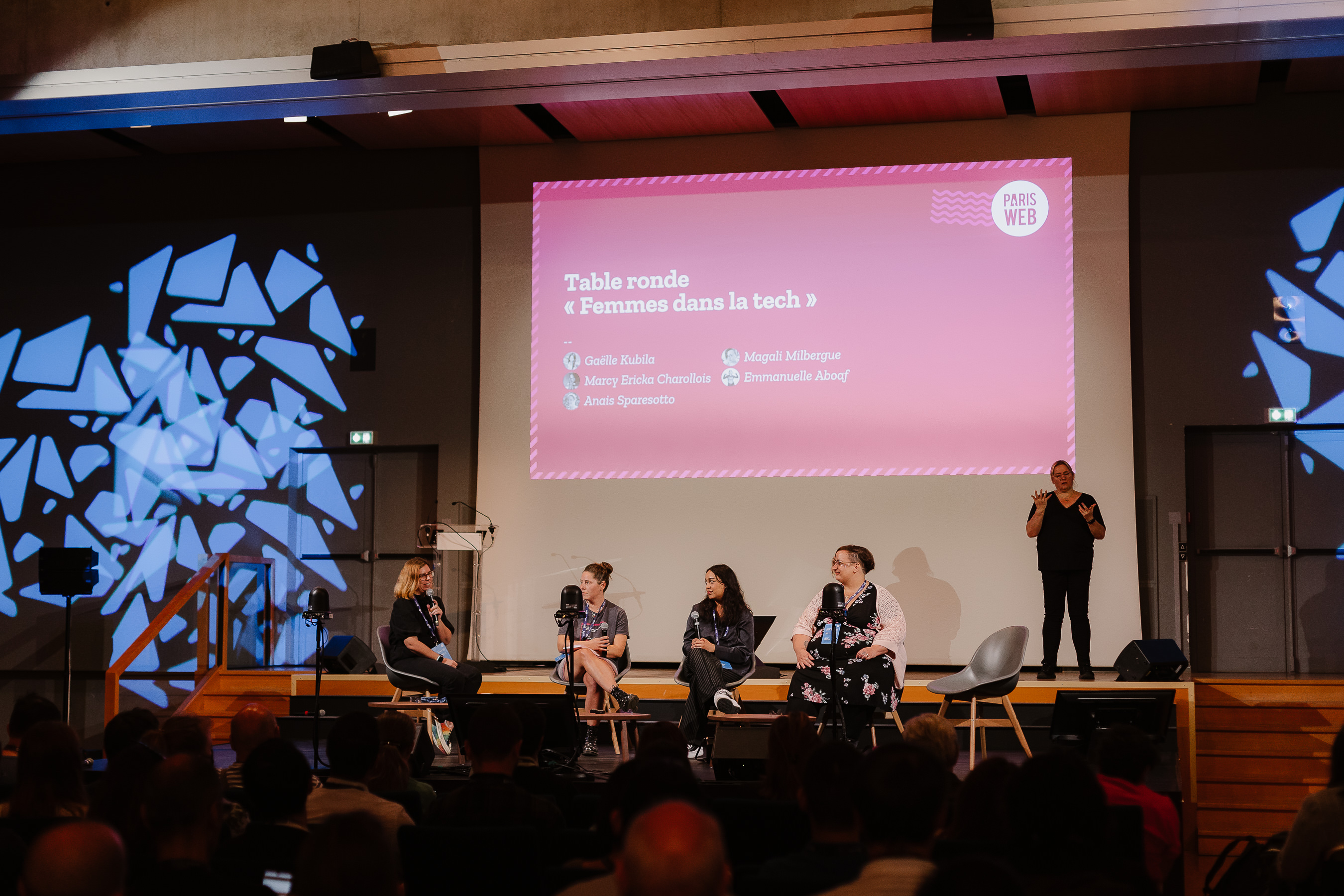 Quatre femmes assises sont sur scène. De gauche à droite : Emmanuelle qui est en train de prendre la parole, Anais, Marcy et Magali qui la regardent en train de parler. Derrière elles, il y a une interprète LSF et l'écran où est projeté Table ronde Femme dans la tech.