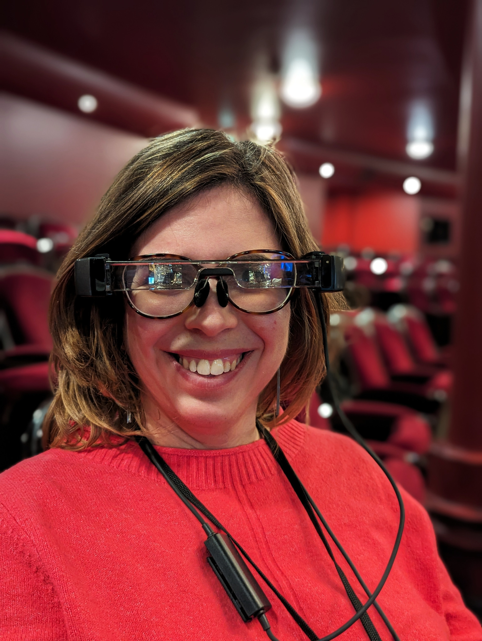 On m'a prise en photo avec les lunettes connectées posées sur mes lunettes. Je suis souriante et habillée en pull rose.